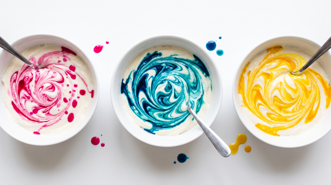 Overhead view of pink, blue and yellow colour swirling into three bowls of white frosting