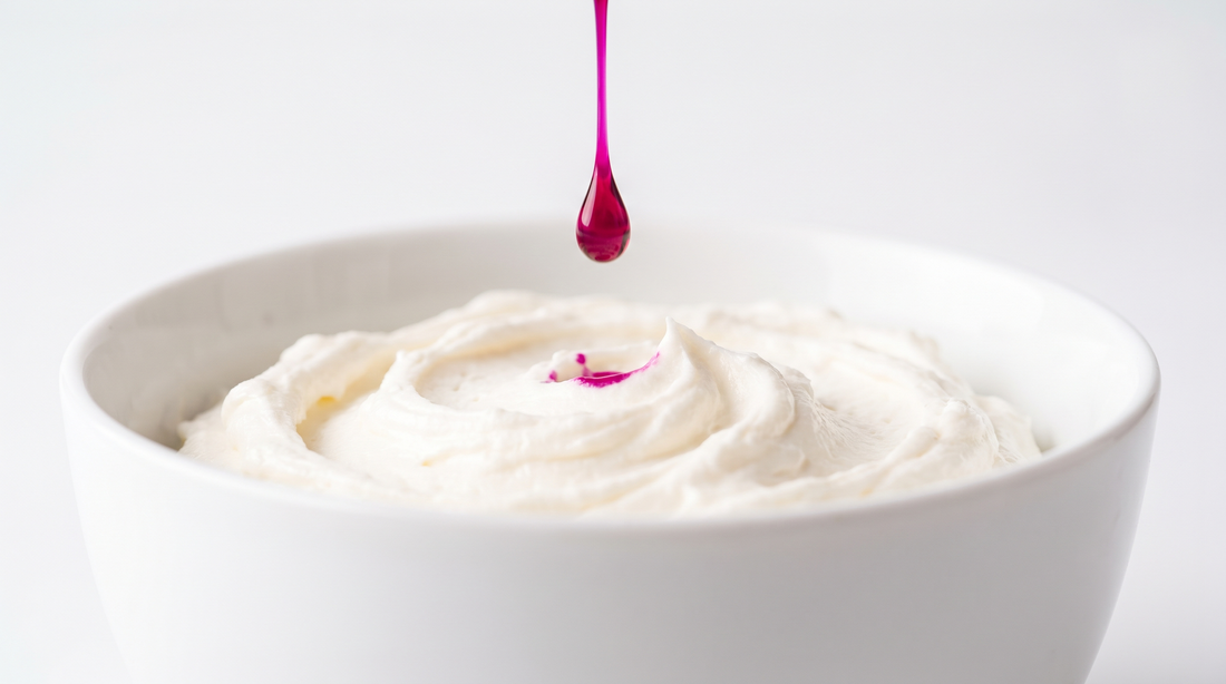 A single drop of vivid magenta colour falling into a bowl of white buttercream