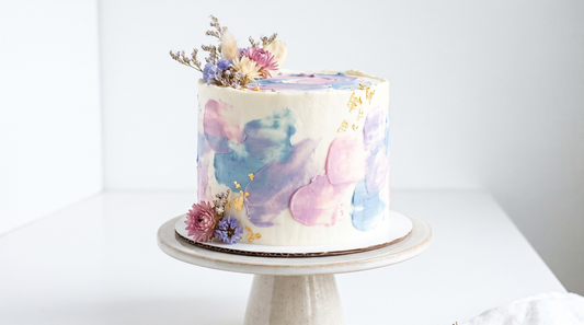 A watercolor effect buttercream cake with soft blended streaks of blue, lilac and pink