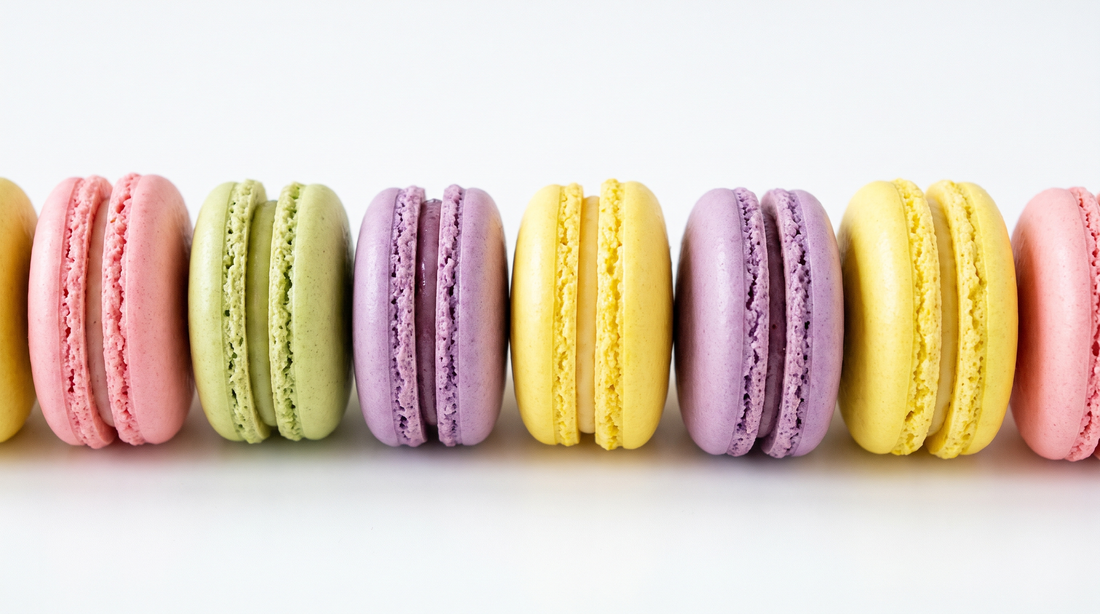 A row of French macarons in pastel pink, pistachio, lilac and lemon with smooth shells