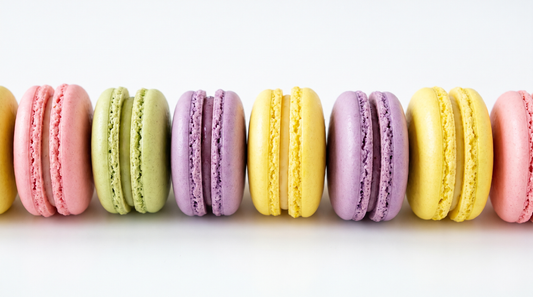A row of French macarons in pastel pink, pistachio, lilac and lemon with smooth shells