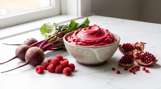 A bowl of naturally red-pink frosting beside fresh beets, raspberries and pomegranate