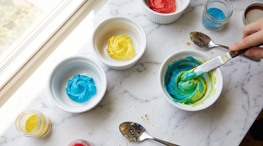 Small bowls of primary colored frosting being blended into new custom shades